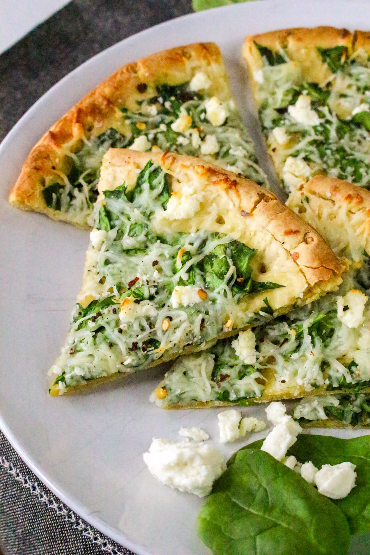 Slices of spinach and feta pizza with a golden crust on a white plate.