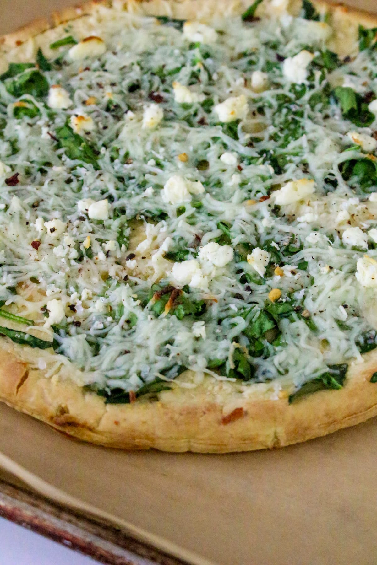 A pizza topped with spinach, cheese, and herbs on a parchment-lined baking sheet.