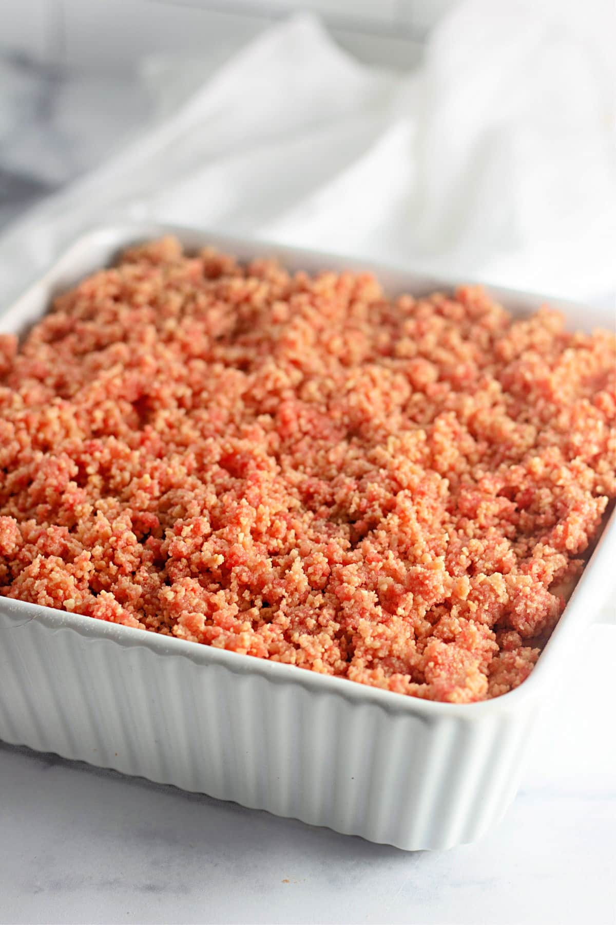 A white ceramic dish filled with uncooked, crumbly, pinkish-brown mixture on a marble countertop.