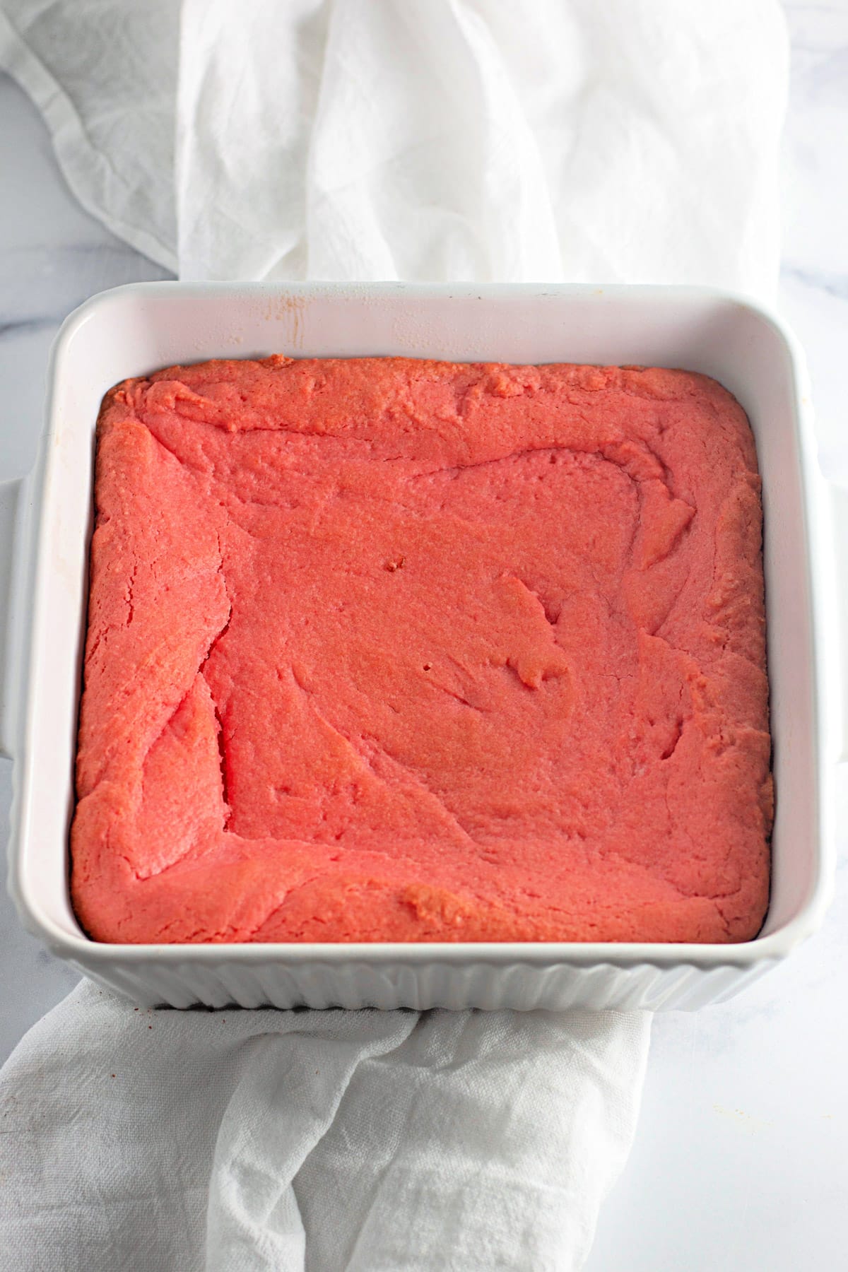 A square baking dish filled with pink cornbread on a white cloth.