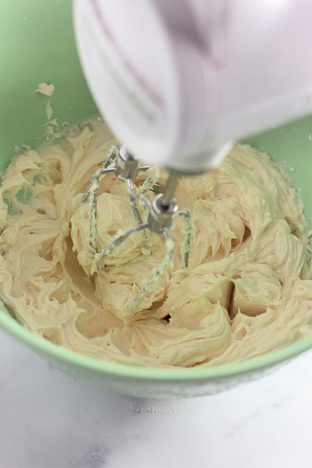 Creamy batter being mixed in a green bowl with an electric hand mixer.