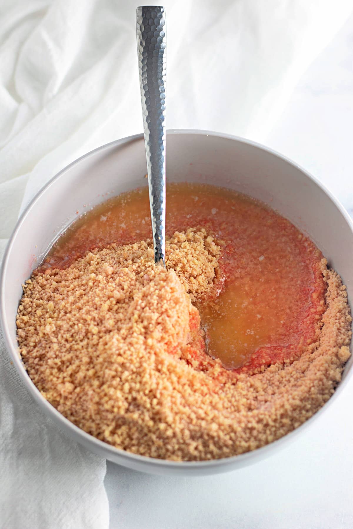 Mixing breadcrumbs into a liquid in a white bowl with a textured metal spoon.