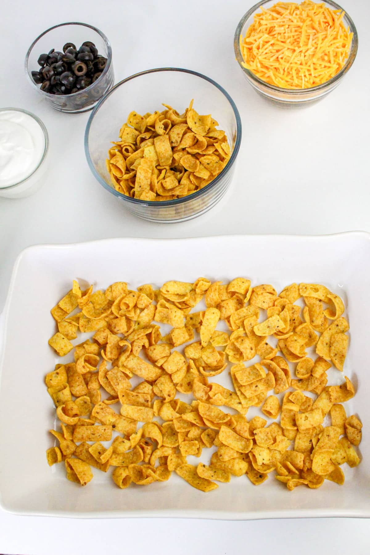Baking dish with corn chips; bowls of black olives, shredded cheese, and sour cream on the side.