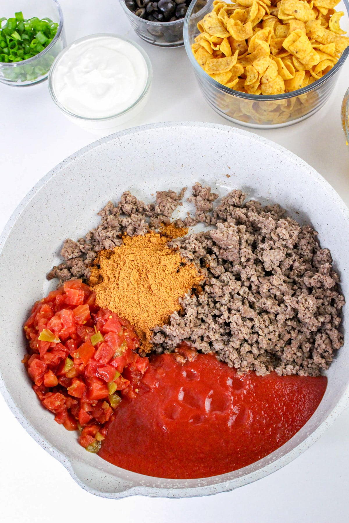 Ingredients for taco casserole in a pot, including ground beef, tomato sauce, diced tomatoes, and taco seasoning.