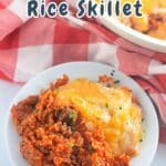 A taco rice skillet sizzles on a red checkered cloth, lavishly topped with melted cheese.