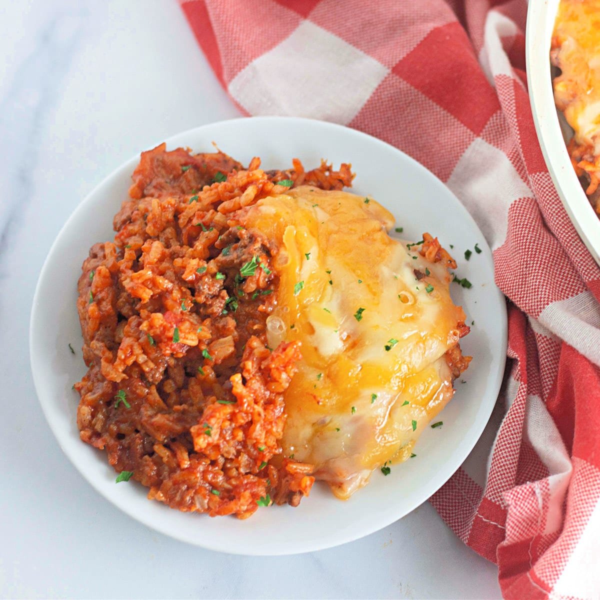 A plate of cheesy skillet rice with beef and tomato sauce, garnished with parsley, on a red and white checkered cloth.