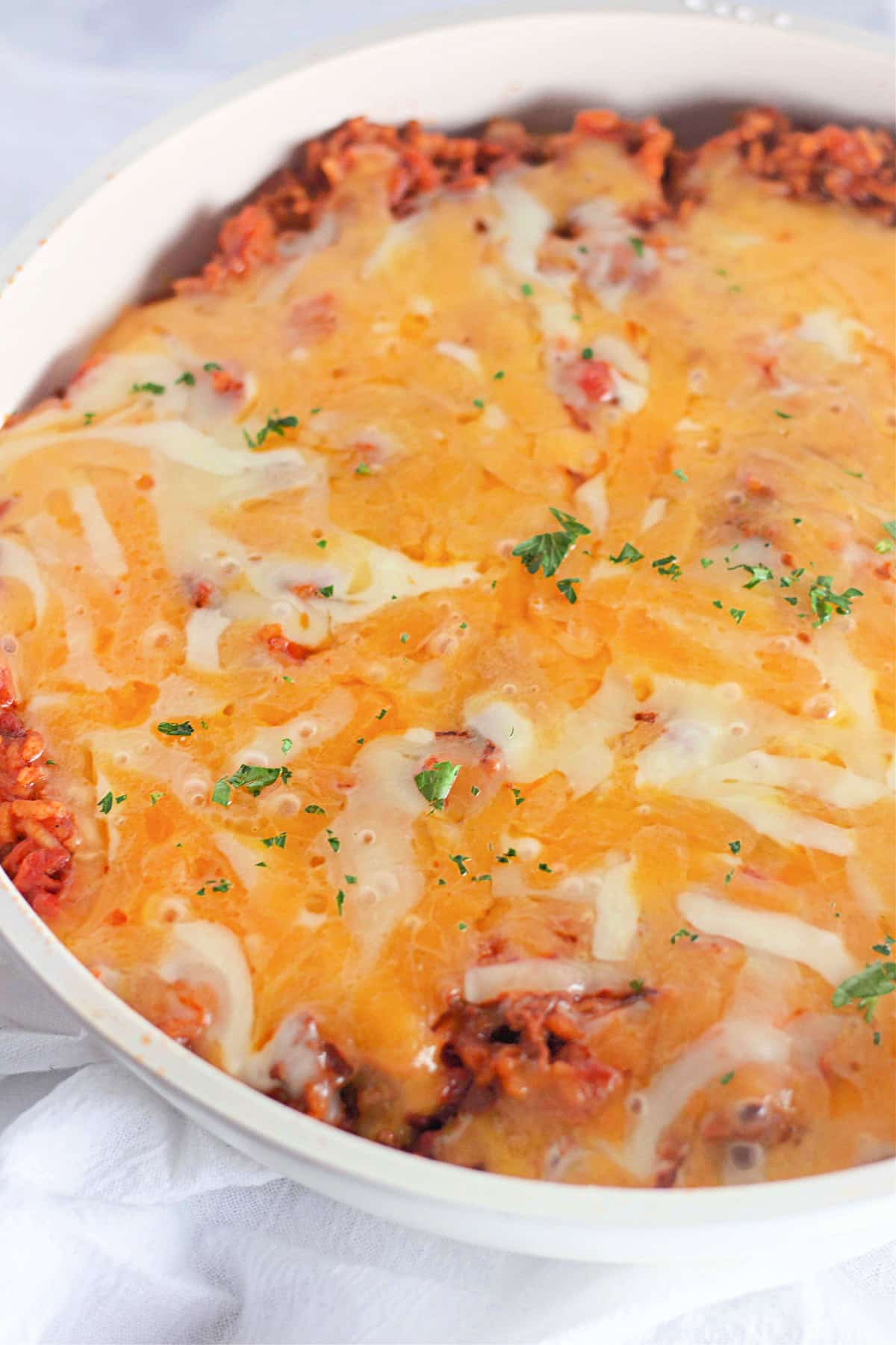 Baked casserole topped with melted cheese and sprinkled with parsley in a white dish.