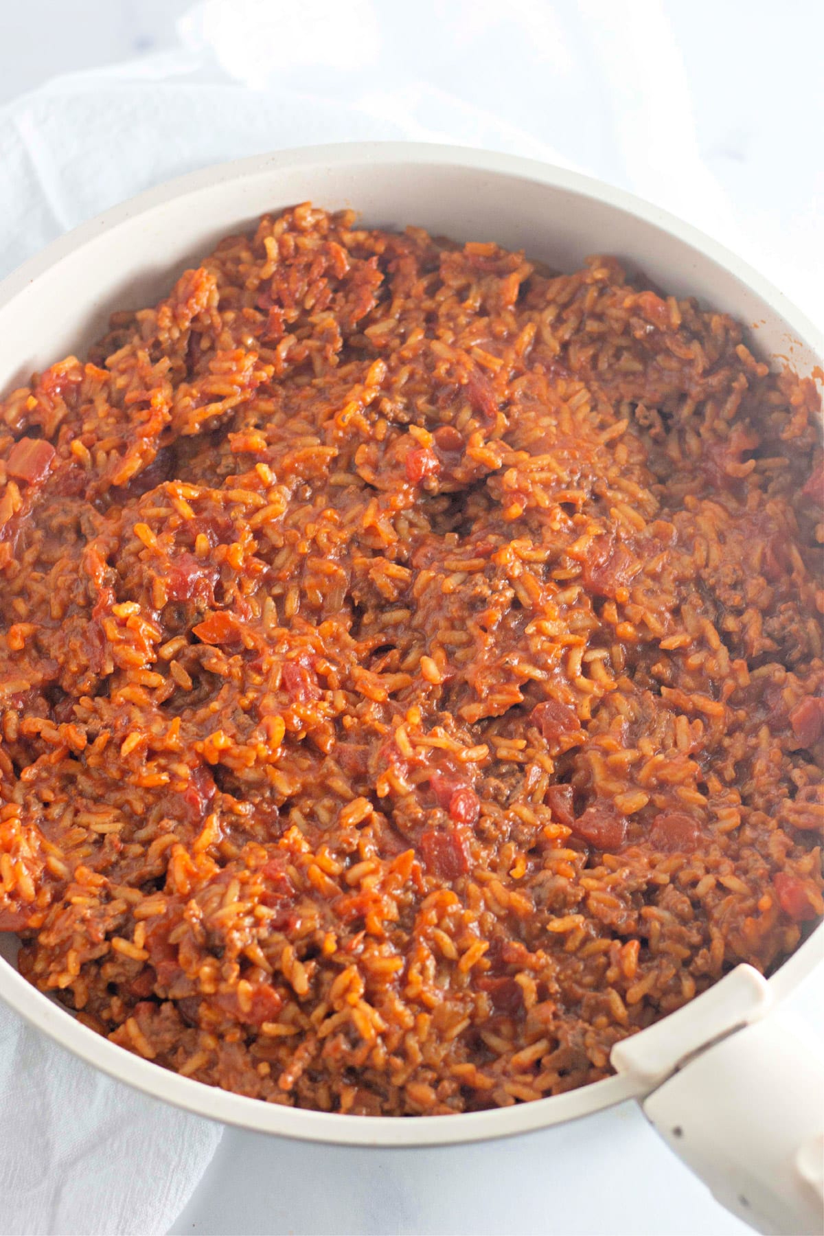 A pot filled with cooked ground beef and tomato rice on a white surface.