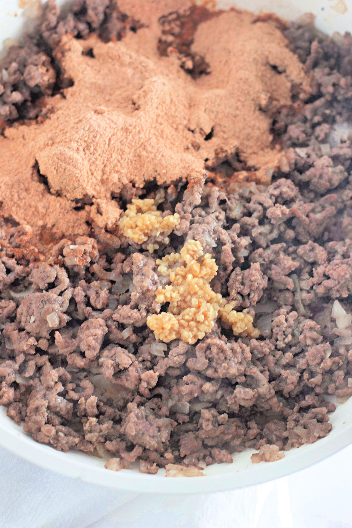 Ground beef cooking in a pan with minced garlic and brown seasoning powder on top.