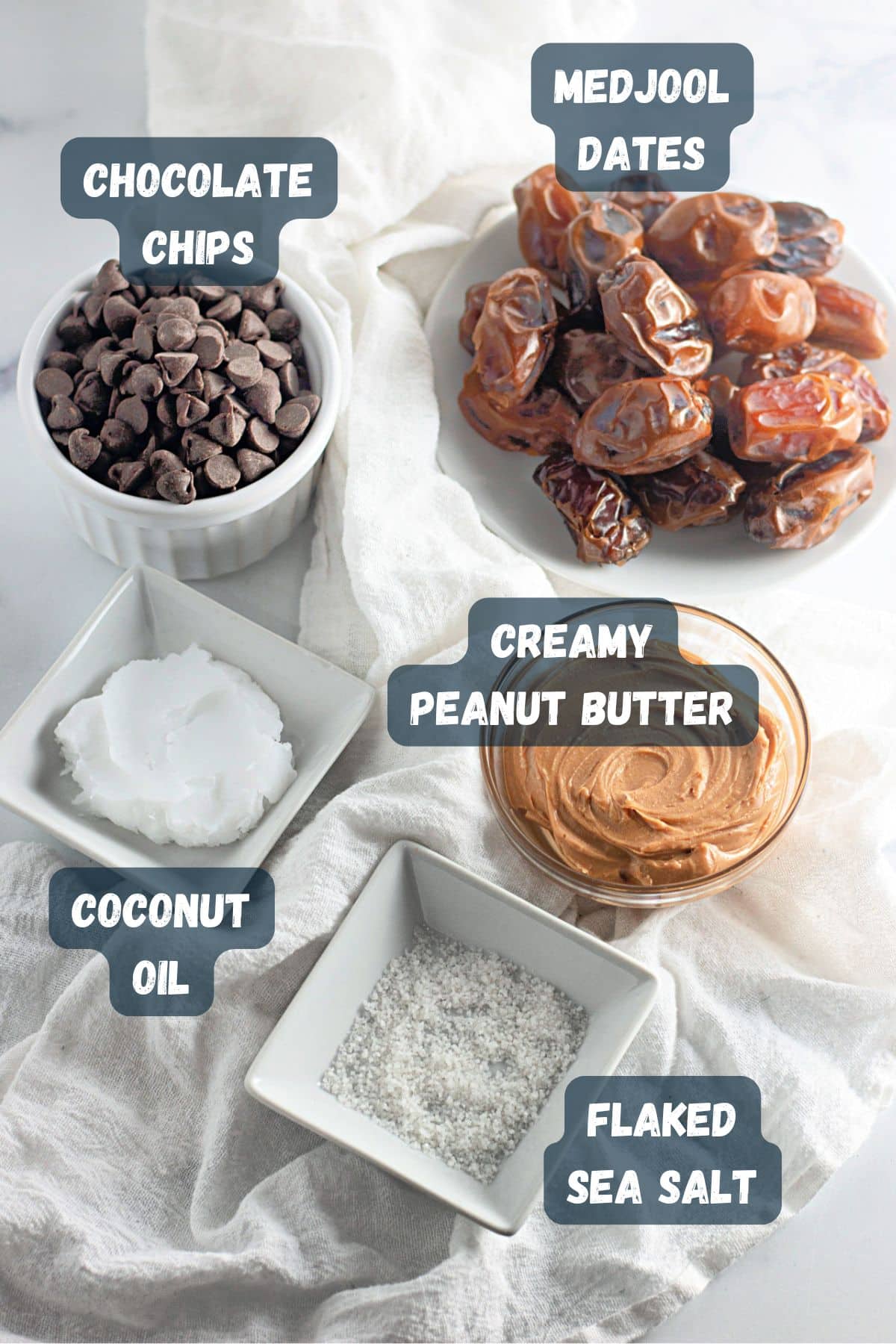 Assorted ingredients on a cloth: chocolate chips, Medjool dates, peanut butter, coconut oil, and flaked sea salt.