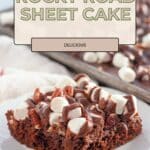 A slice of Rocky Road Cake sheet cake topped with marshmallows, pecans, and chocolate sits on a white plate.