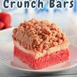 A delightful square strawberry crunch bar with a crumb topping rests invitingly on a plate, set against the backdrop of a rustic wooden table.