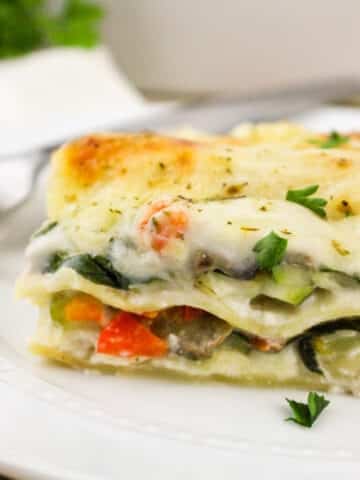 A slice of vegetable lasagna topped with fresh herbs on a white plate.