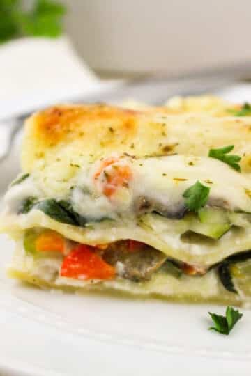 A slice of vegetable lasagna topped with fresh herbs on a white plate.