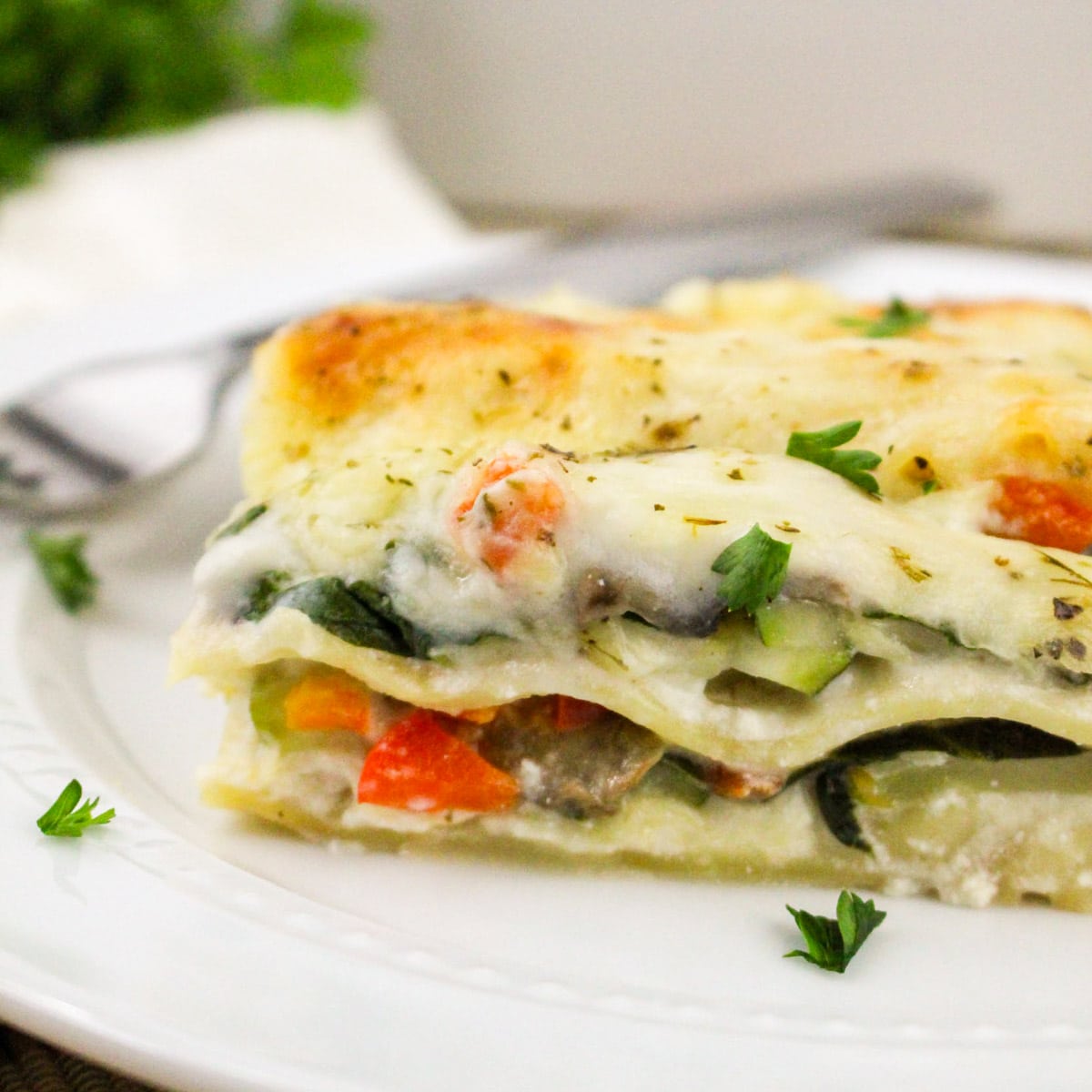 A slice of vegetable lasagna topped with fresh herbs on a white plate.