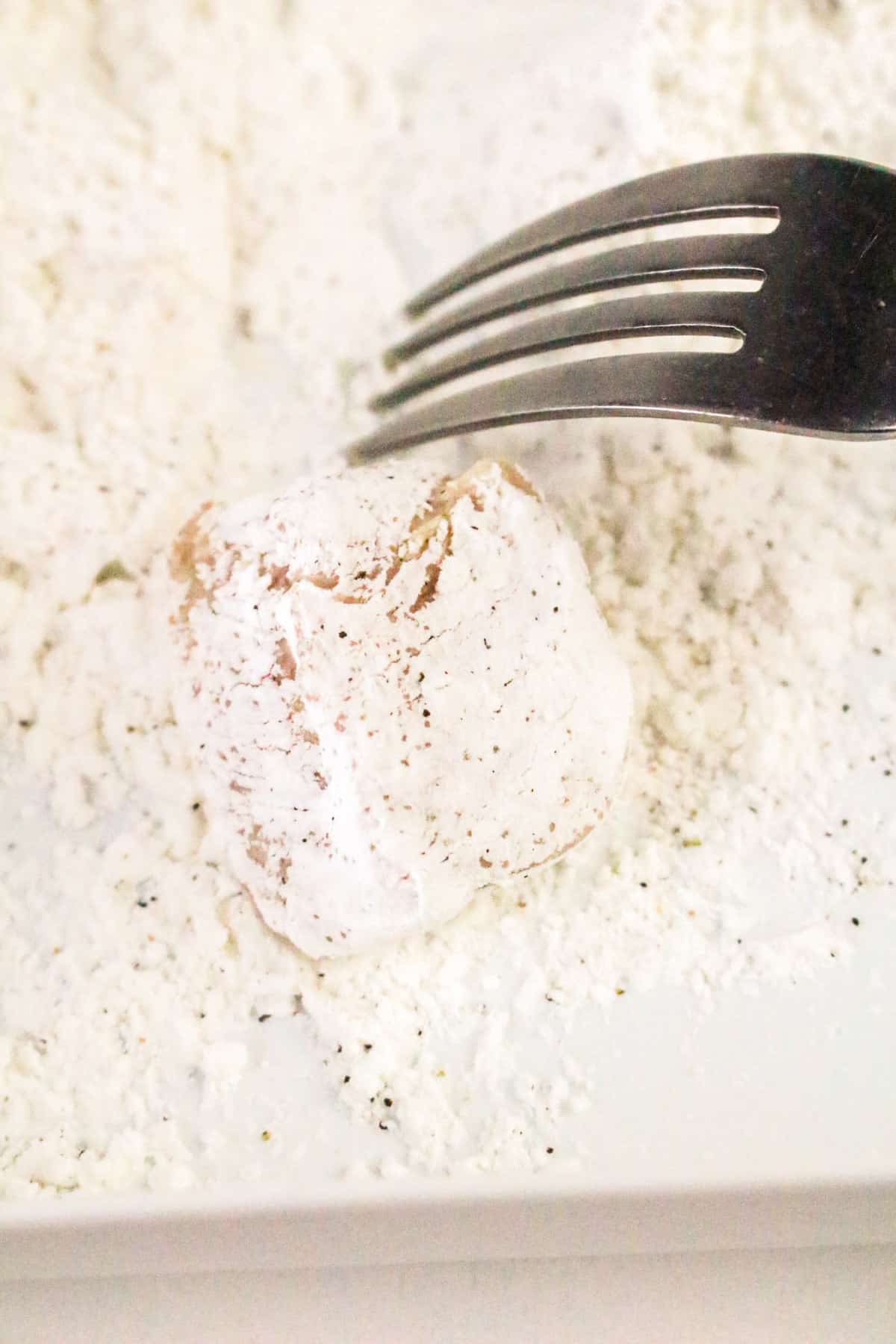 A fork rests beside a dough ball coated in white flour on a floured surface.