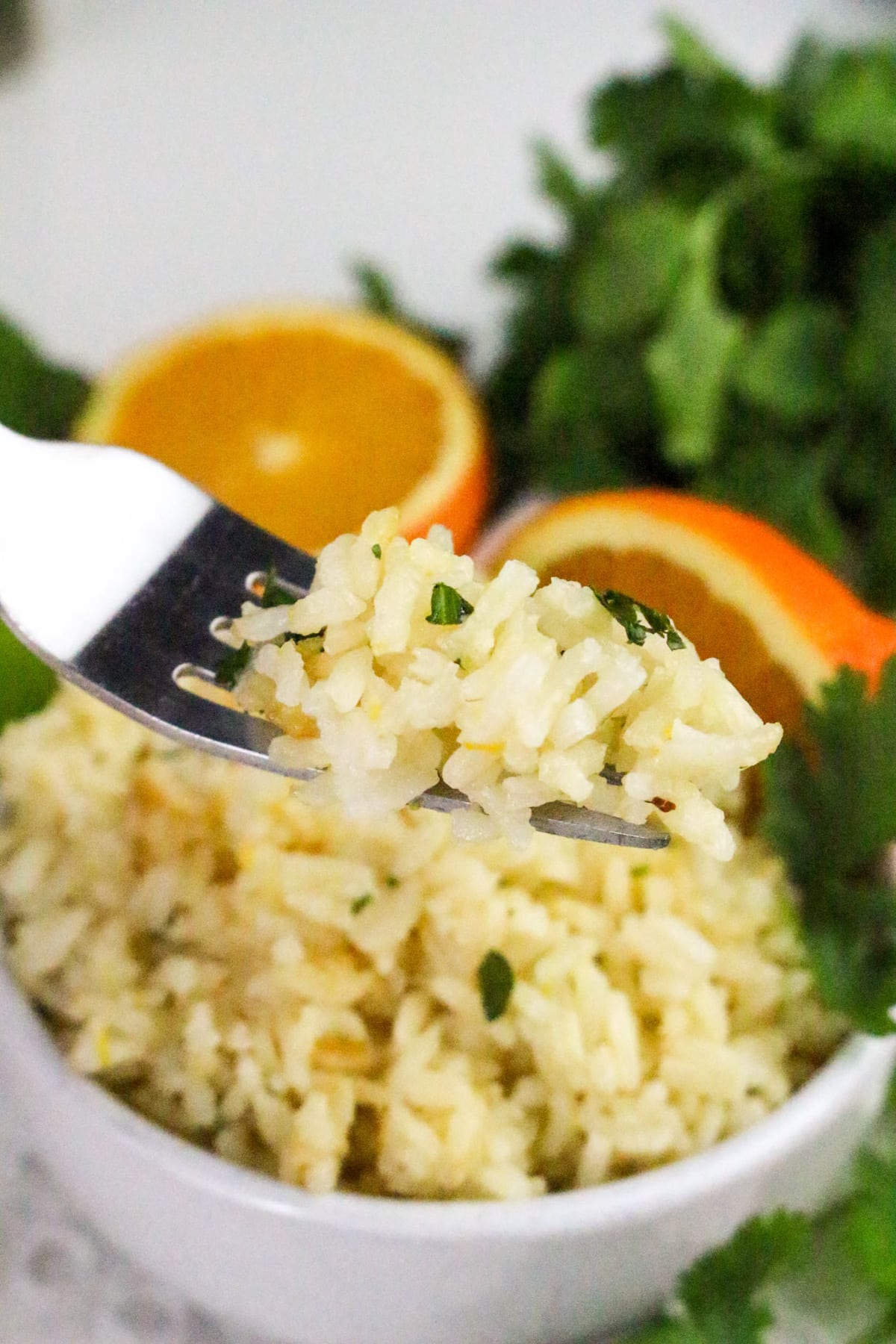 Fork with seasoned rice above a bowl, garnished with herbs. Sliced orange and cilantro in the background.