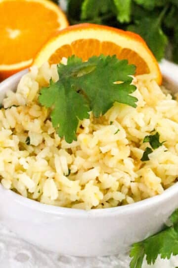 Bowl of rice garnished with cilantro, surrounded by orange slices, lime, and cilantro bunch.