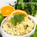 A vibrant bowl of citrus rice garnished with a cilantro leaf and orange slice sits invitingly, surrounded by fresh oranges and lime in the background.