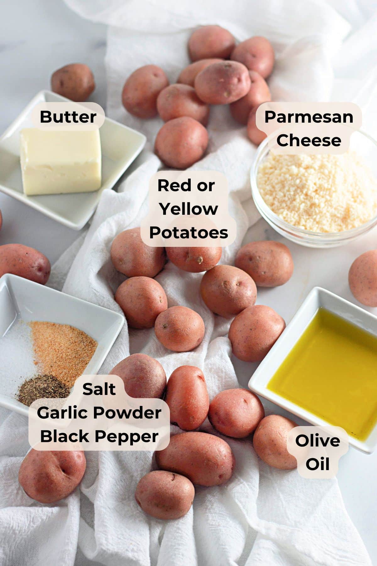 Red potatoes, butter, olive oil, and seasonings come together for a delicious garlic parmesan smashed potatoes dish, beautifully arranged on a white cloth background.
