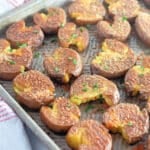 Crispy smashed potatoes with herbs on a baking sheet.