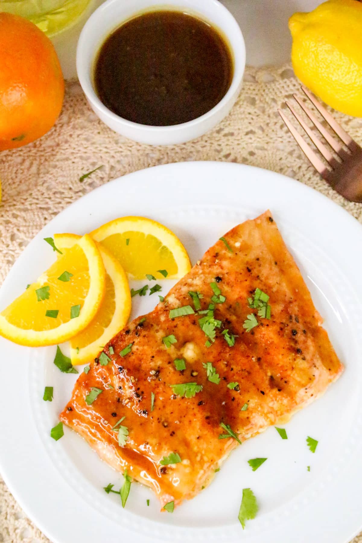 Grilled salmon garnished with parsley and orange slices on a white plate, with a small bowl of sauce beside it.