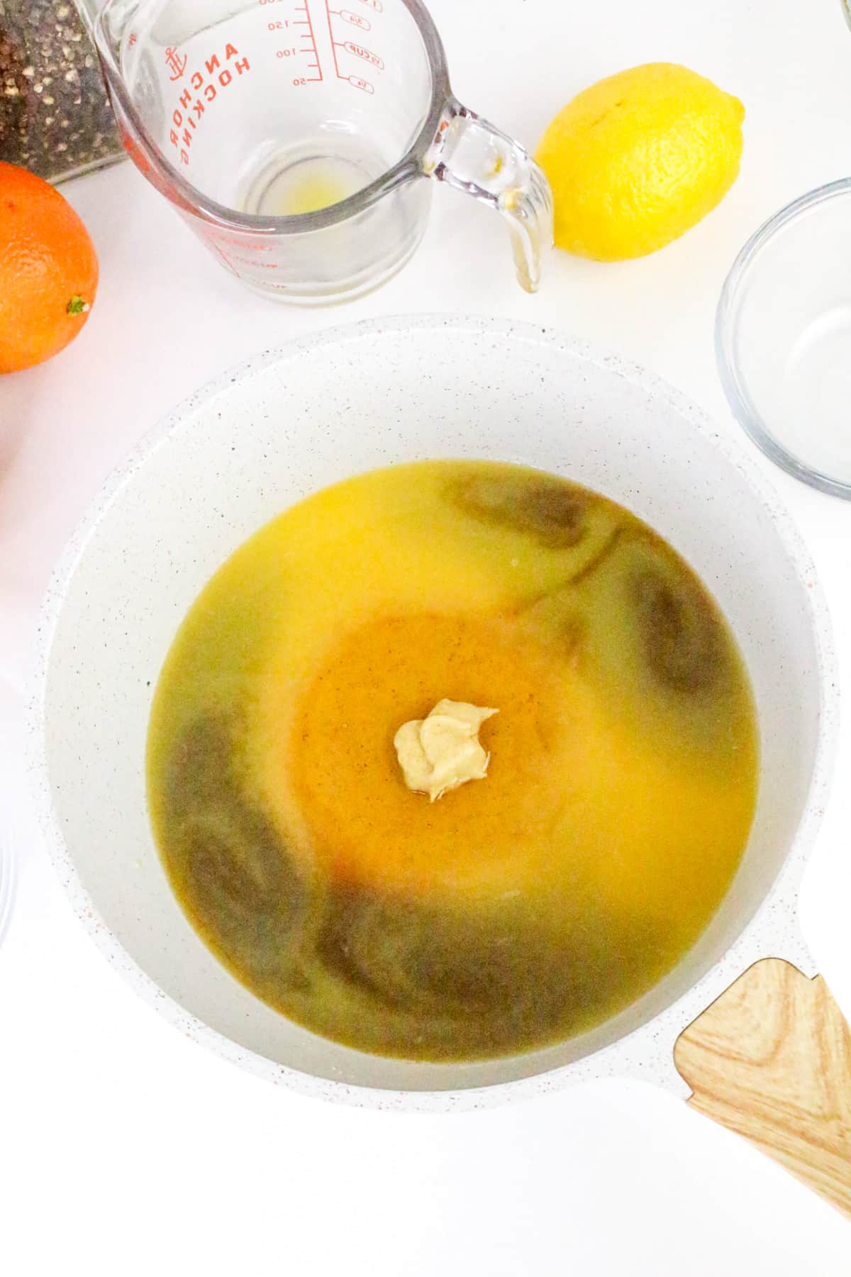 A mixture of ingredients in a white bowl, surrounded by a lemon, orange, measuring cup, and spices.