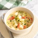 A bowl of creamy soup with vegetables, on a table with a spoon and checkered cloth.