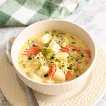 A bowl of creamy soup with vegetables, on a table with a spoon and checkered cloth.