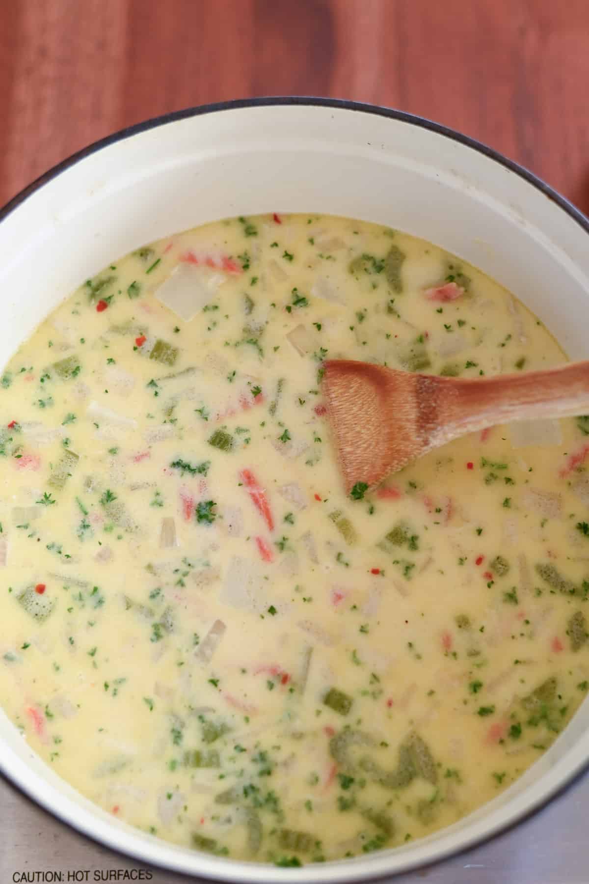 A pot of creamy vegetable soup with visible herbs and a wooden spoon, on a wooden table.