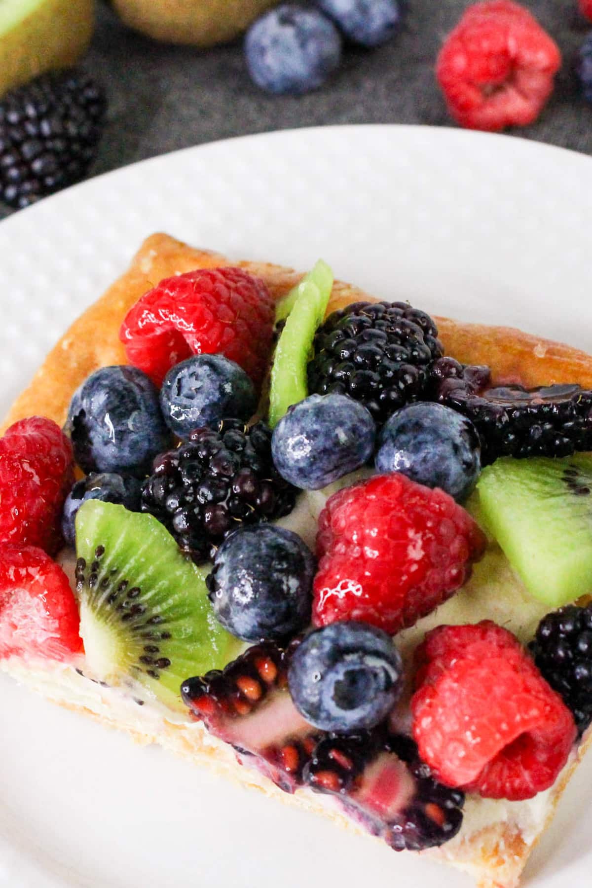 Fruit tart topped with raspberries, blackberries, blueberries, and kiwi slices on a white plate.