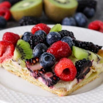 A fruit tart with blueberries, raspberries, blackberries, and kiwi slices on a white plate.