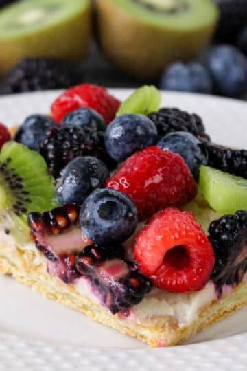 A fruit tart with blueberries, raspberries, blackberries, and kiwi slices on a white plate.