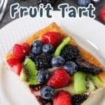 A delicious puff pastry fruit tart graces a white plate, adorned with vibrant kiwi slices, juicy raspberries, plump blueberries, and luscious blackberries.