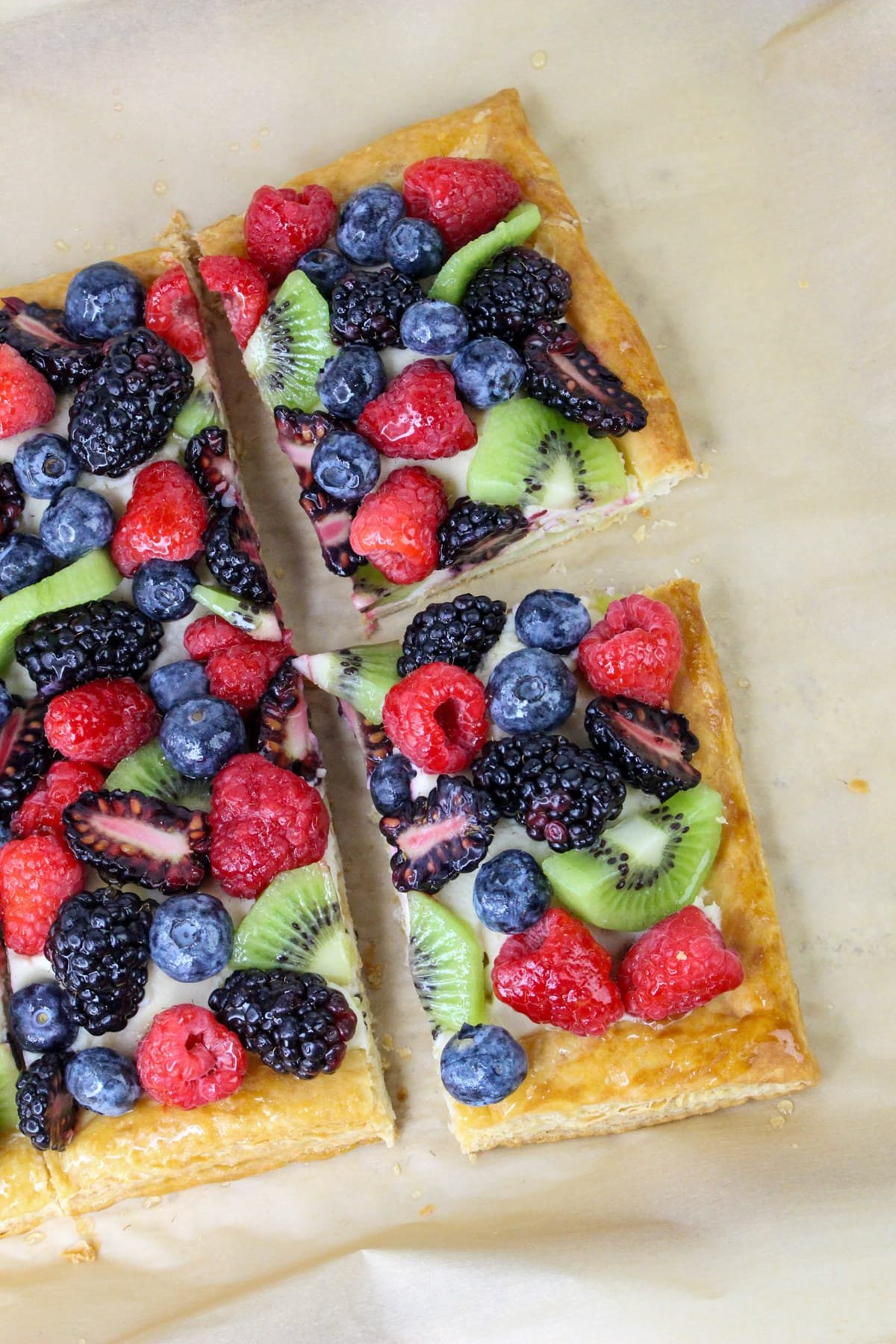 Fruit tart with kiwi, raspberries, blueberries, and blackberries on a cream-filled pastry, cut into squares.