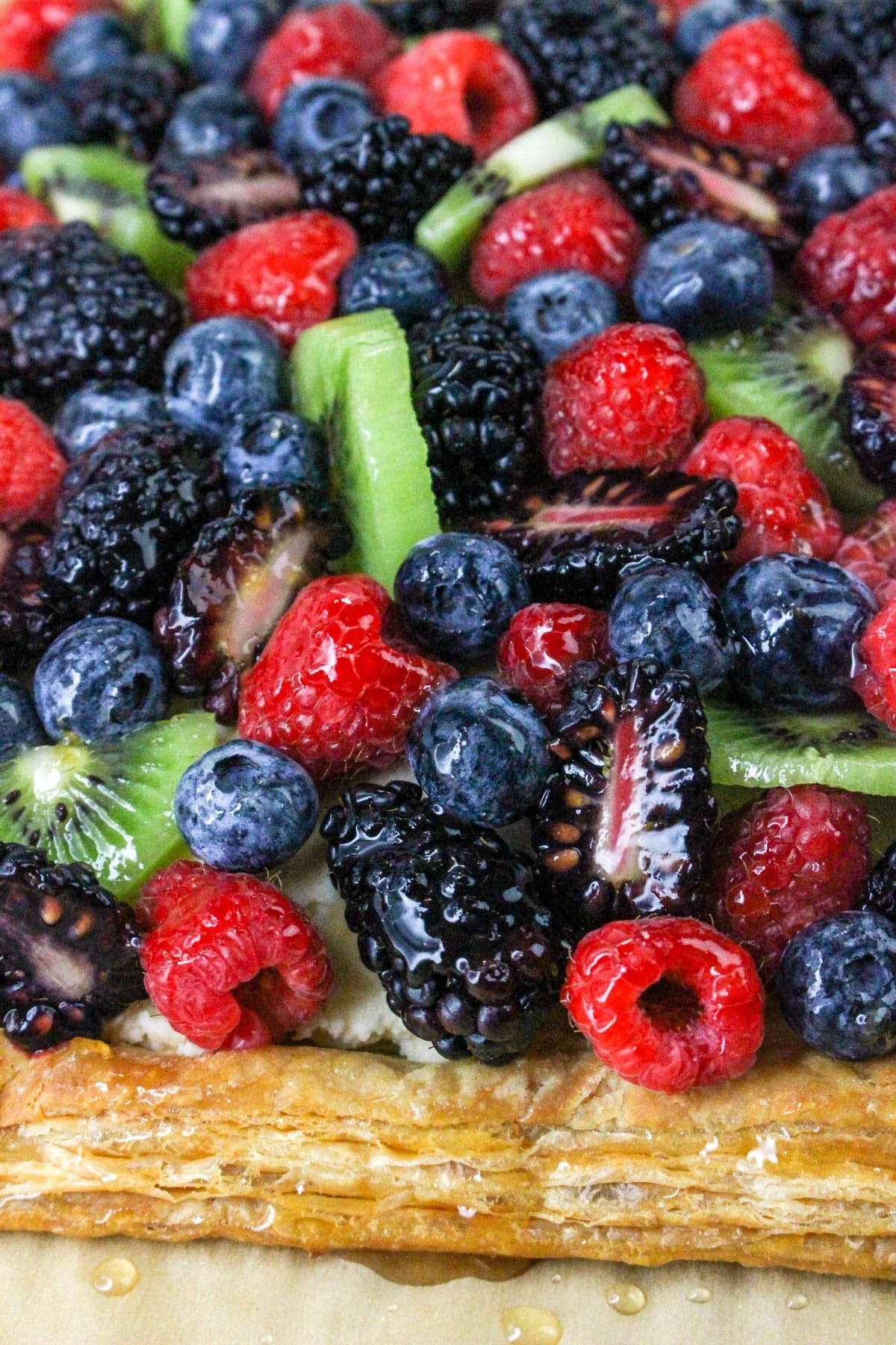 Close-up of a fruit tart topped with blackberries, blueberries, raspberries, and kiwi slices on a pastry crust.