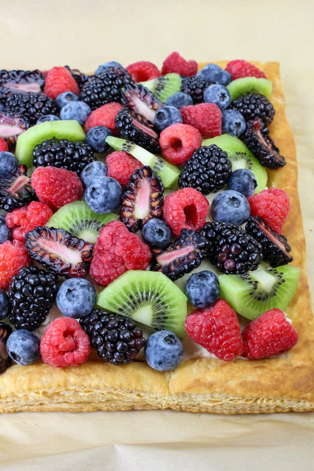 Fruit tart topped with raspberries, blackberries, blueberries, strawberries, and kiwi on a flaky crust.