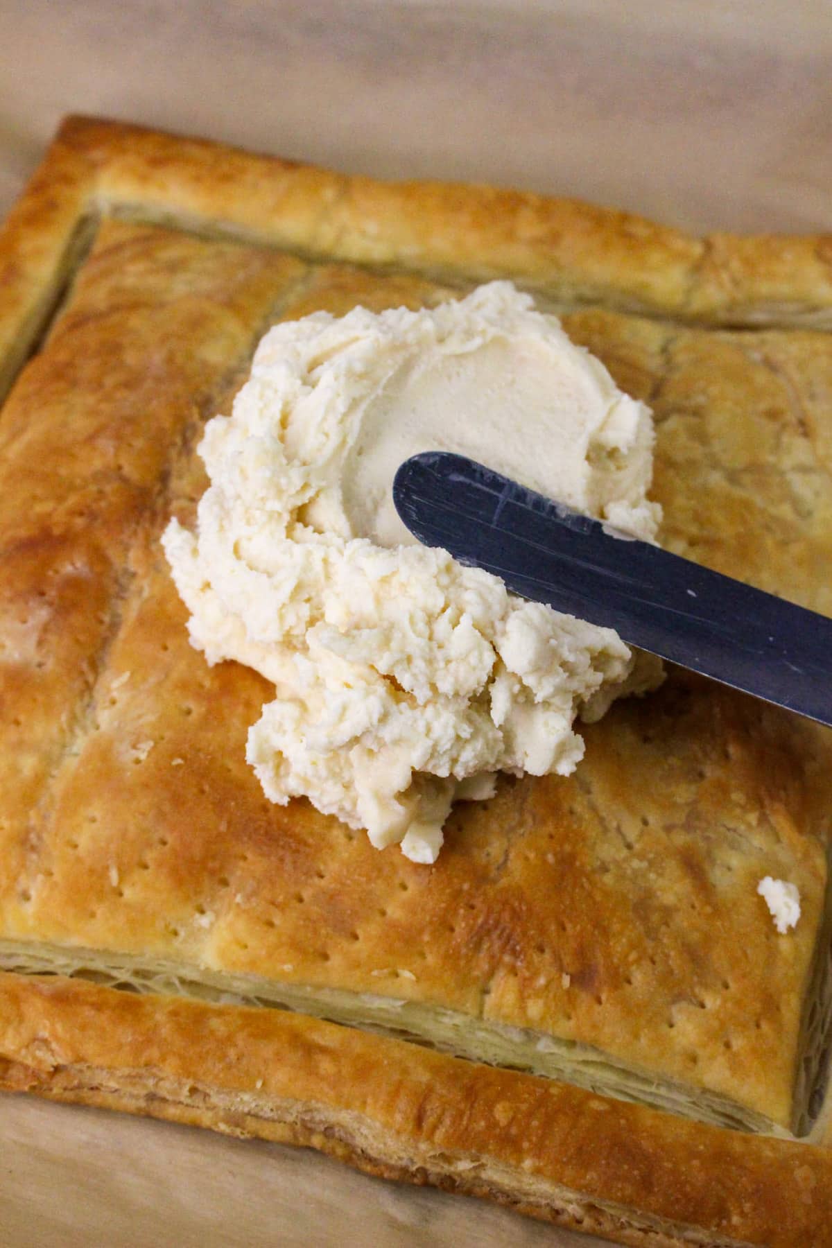 A flaky pastry topped with a scoop of light-colored spread, shown with a spreading knife.