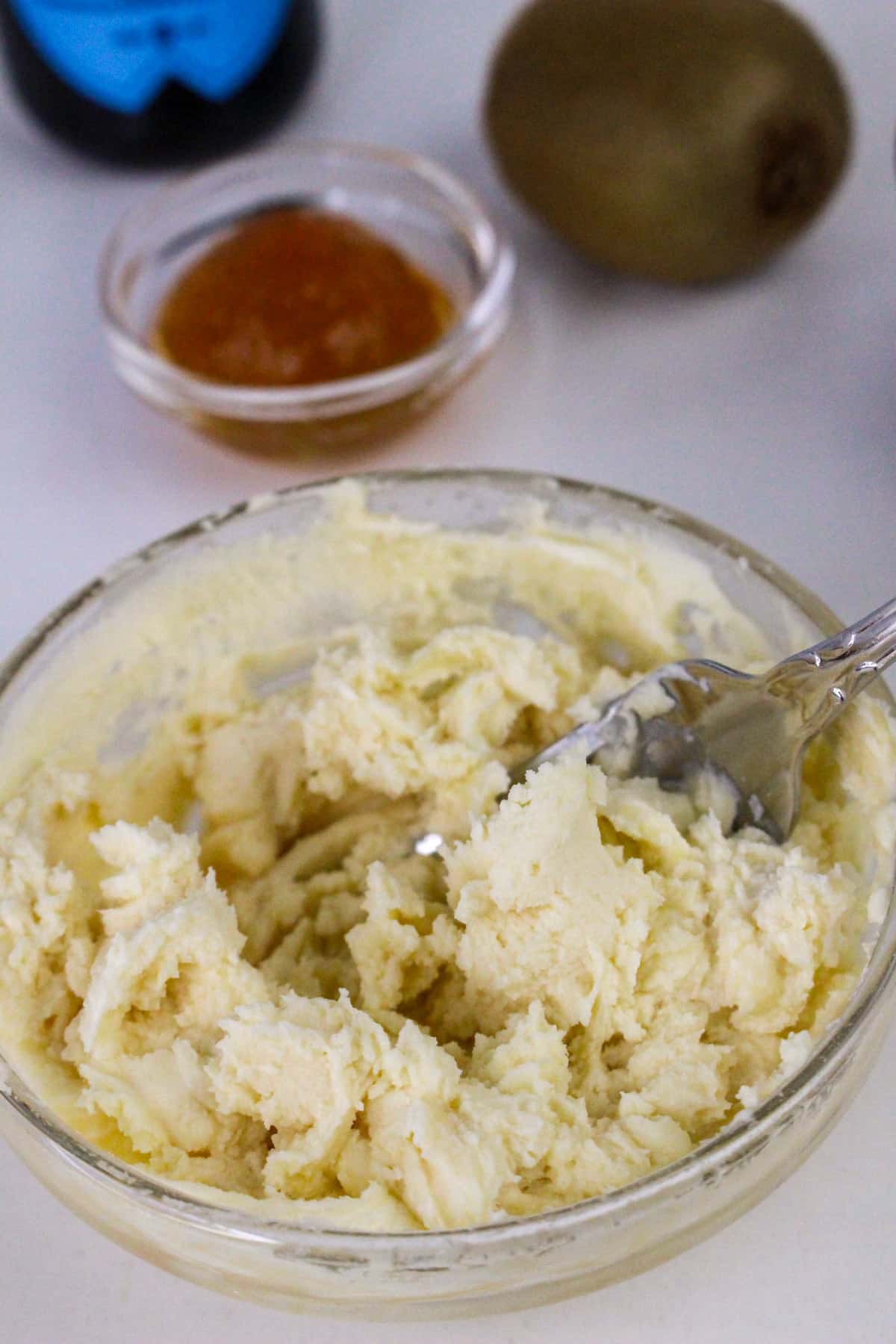 Bowl of creamy dessert with a spoon, kiwi fruit, and caramel sauce in the background.