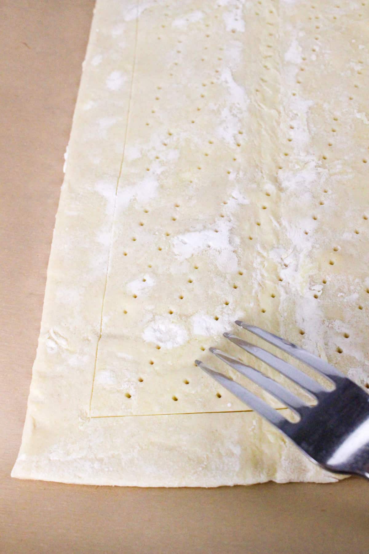 Fork piercing puff pastry dough with small holes on a floured surface.