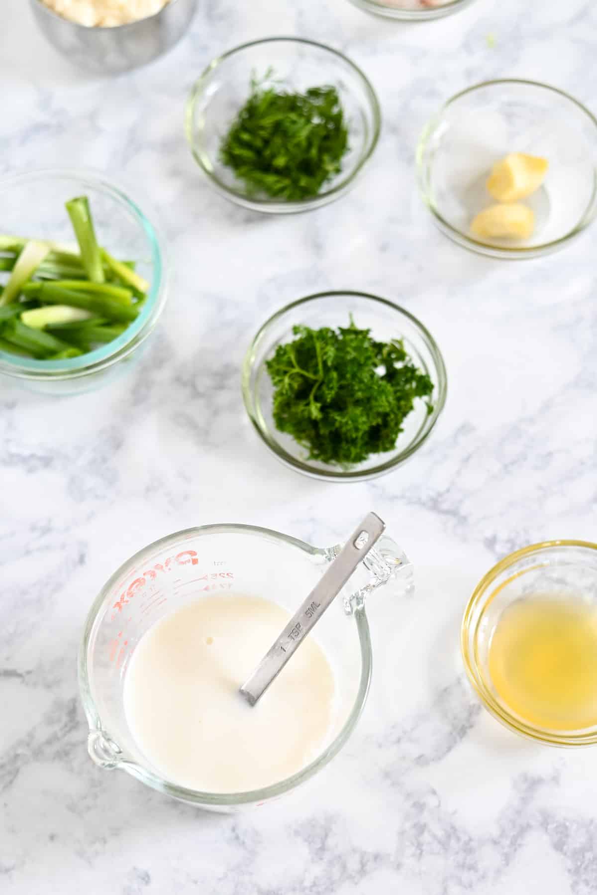 Various glass bowls with milk, herbs, and green onions on a marble countertop.