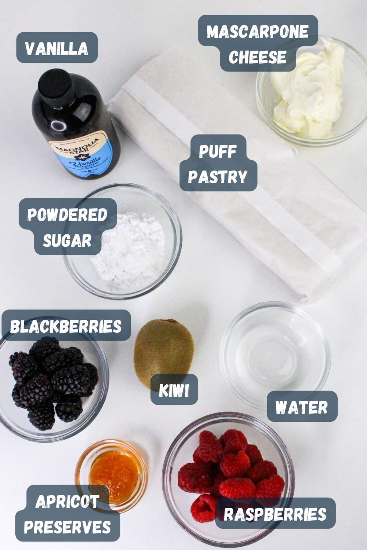 Ingredients for a dessert on a table: vanilla, mascarpone, puff pastry, powdered sugar, berries, kiwi, preserves, water.