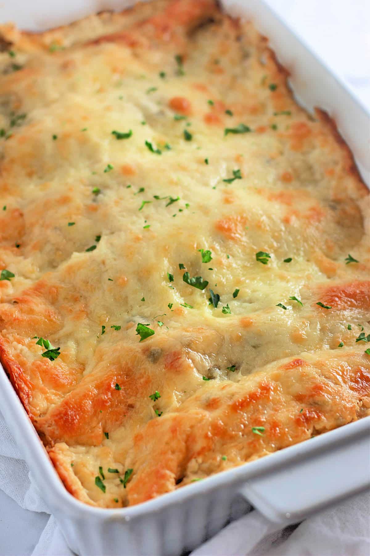 Baked casserole in a white dish topped with melted cheese and sprinkled with parsley.