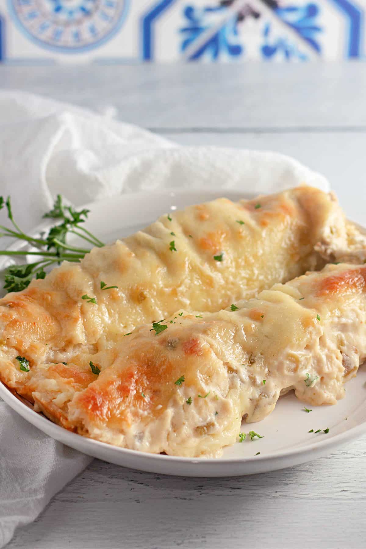 Two creamy stuffed enchiladas on a white plate, garnished with chopped herbs.