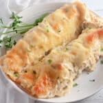 Two baked enchiladas with melted cheese on a white plate, garnished with parsley sprigs.