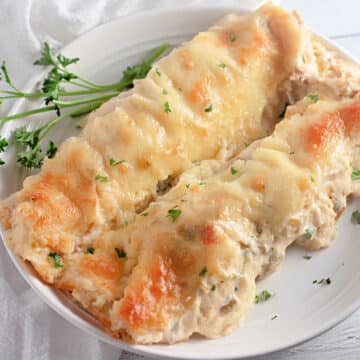Two baked enchiladas with melted cheese on a white plate, garnished with parsley sprigs.