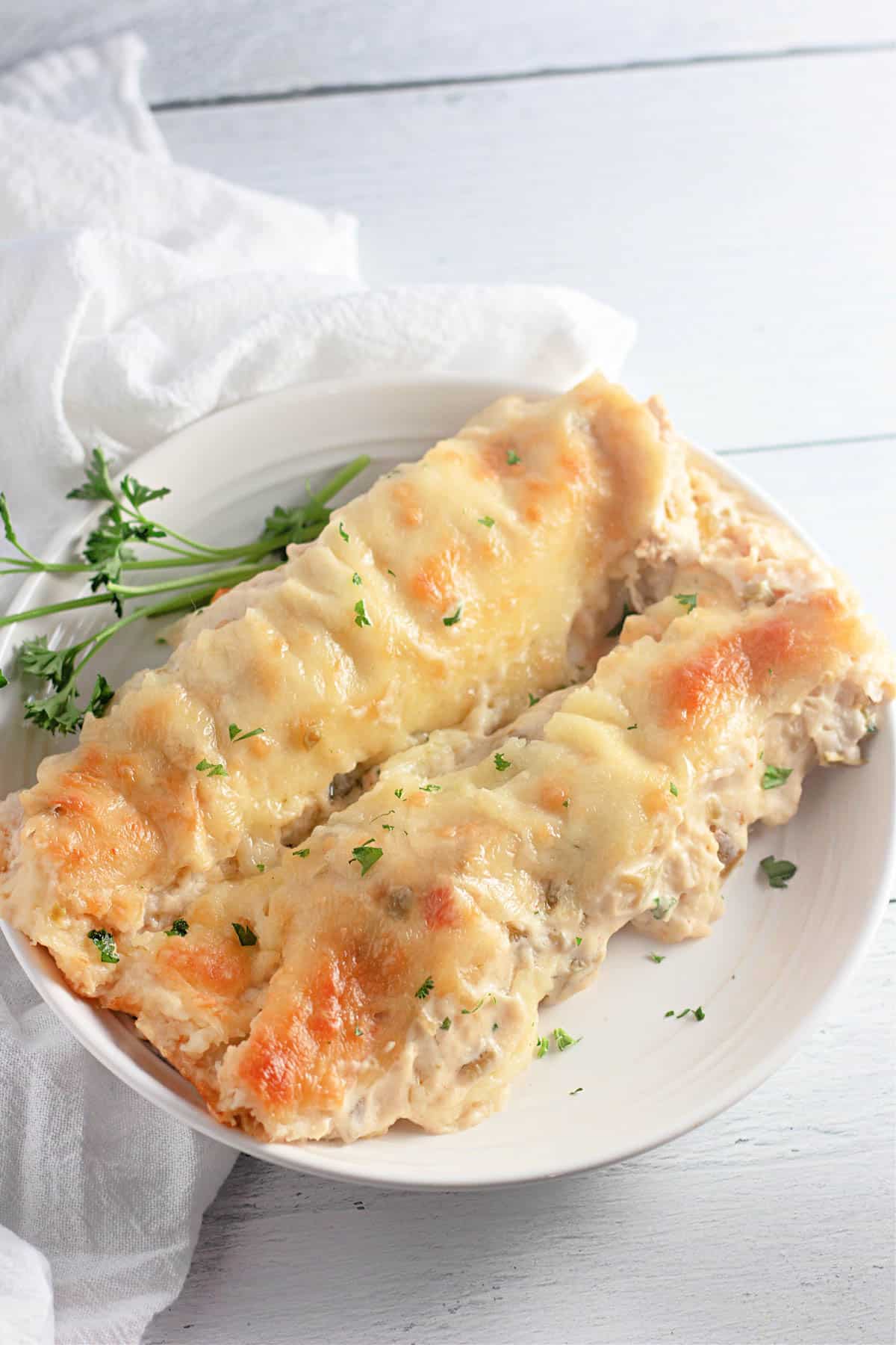 Two cheese-covered enchiladas on a white plate, garnished with parsley.
