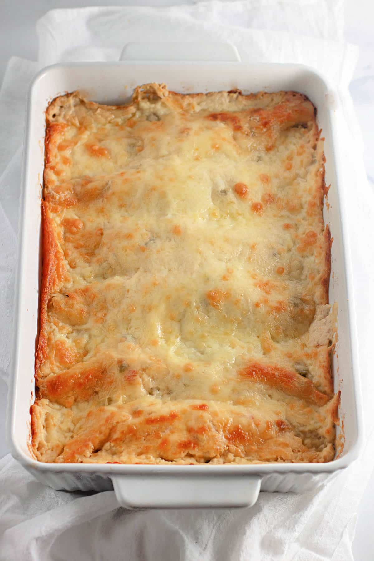 Baked enchiladas with golden melted cheese in a white rectangular dish.