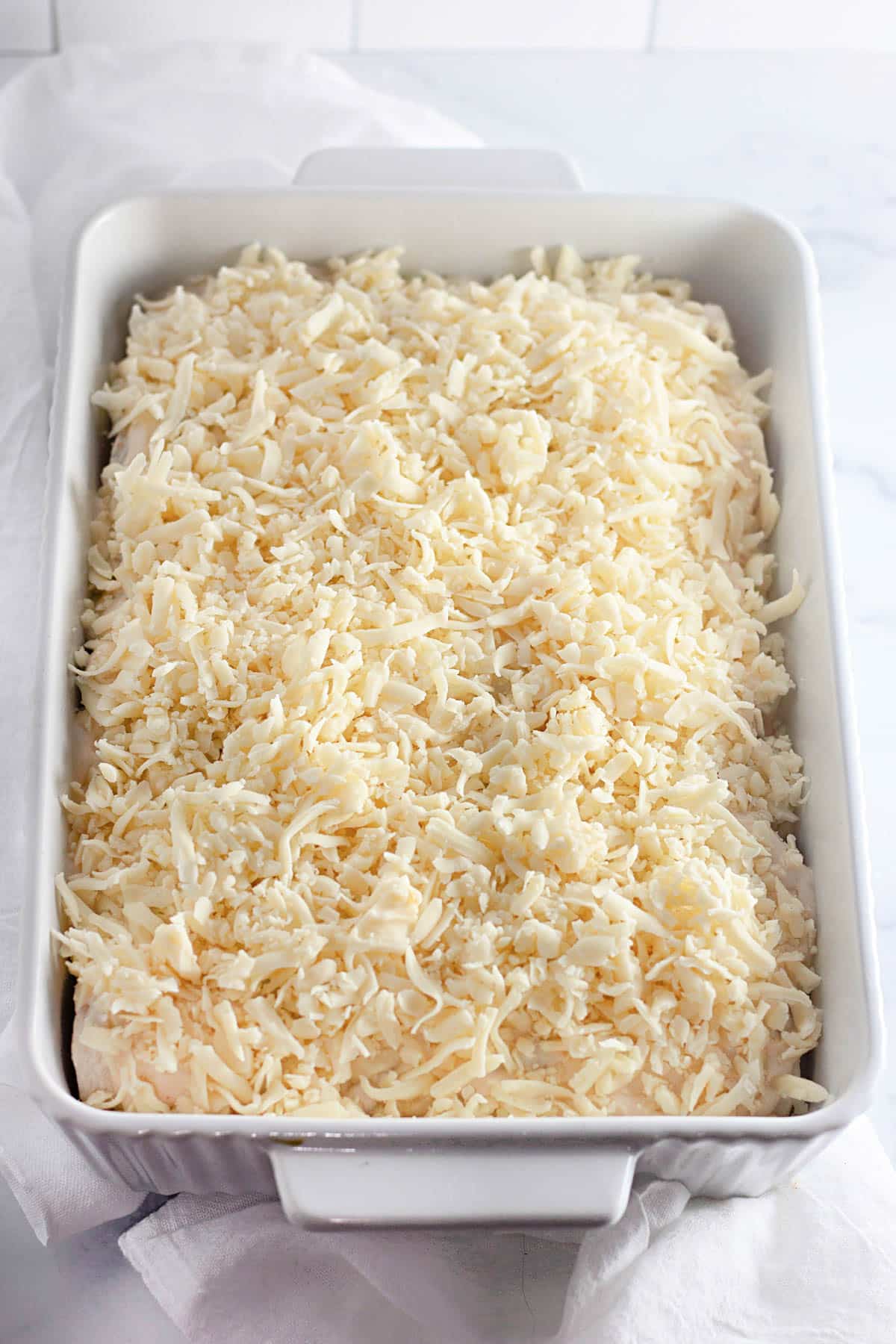 White casserole dish filled with shredded cheese on a light background.