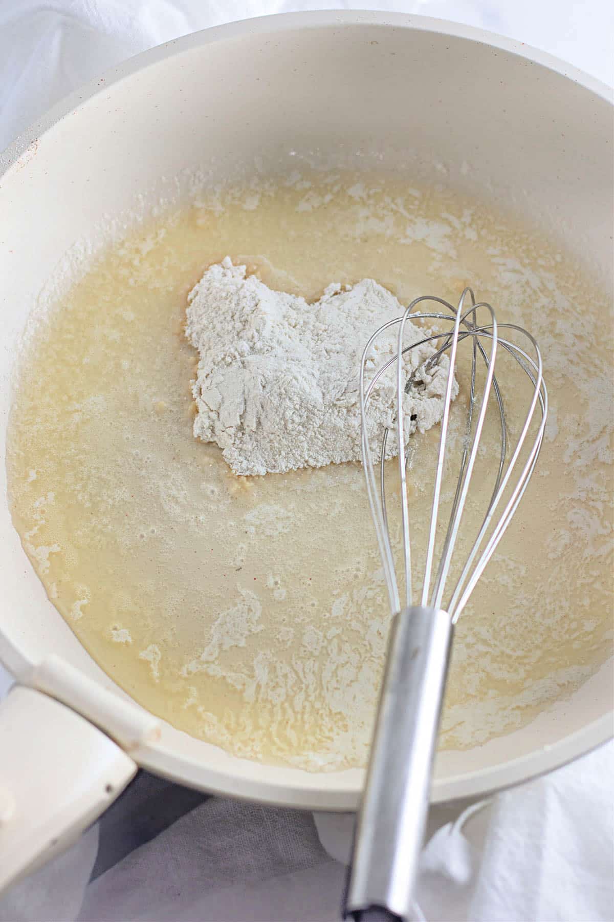 Flour and butter being whisked together in a white skillet.